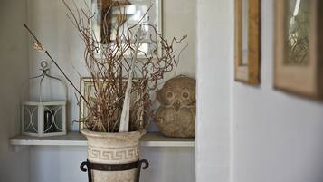 A white vase with a geometric pattern on a pedestal, containing branches and a white candle.