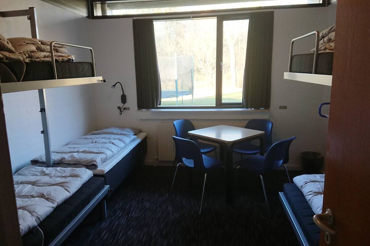 Een kleine kamer met stapelbedden, een tafeltje en stoelen.