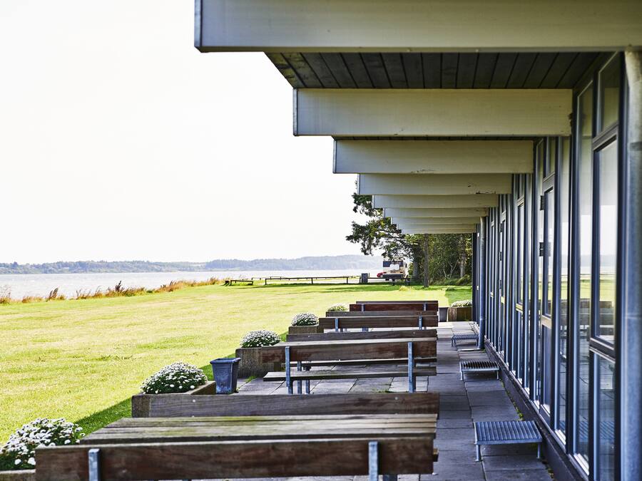 A covered outdoor seating area with benches, a view of the water, and a building with large windows.