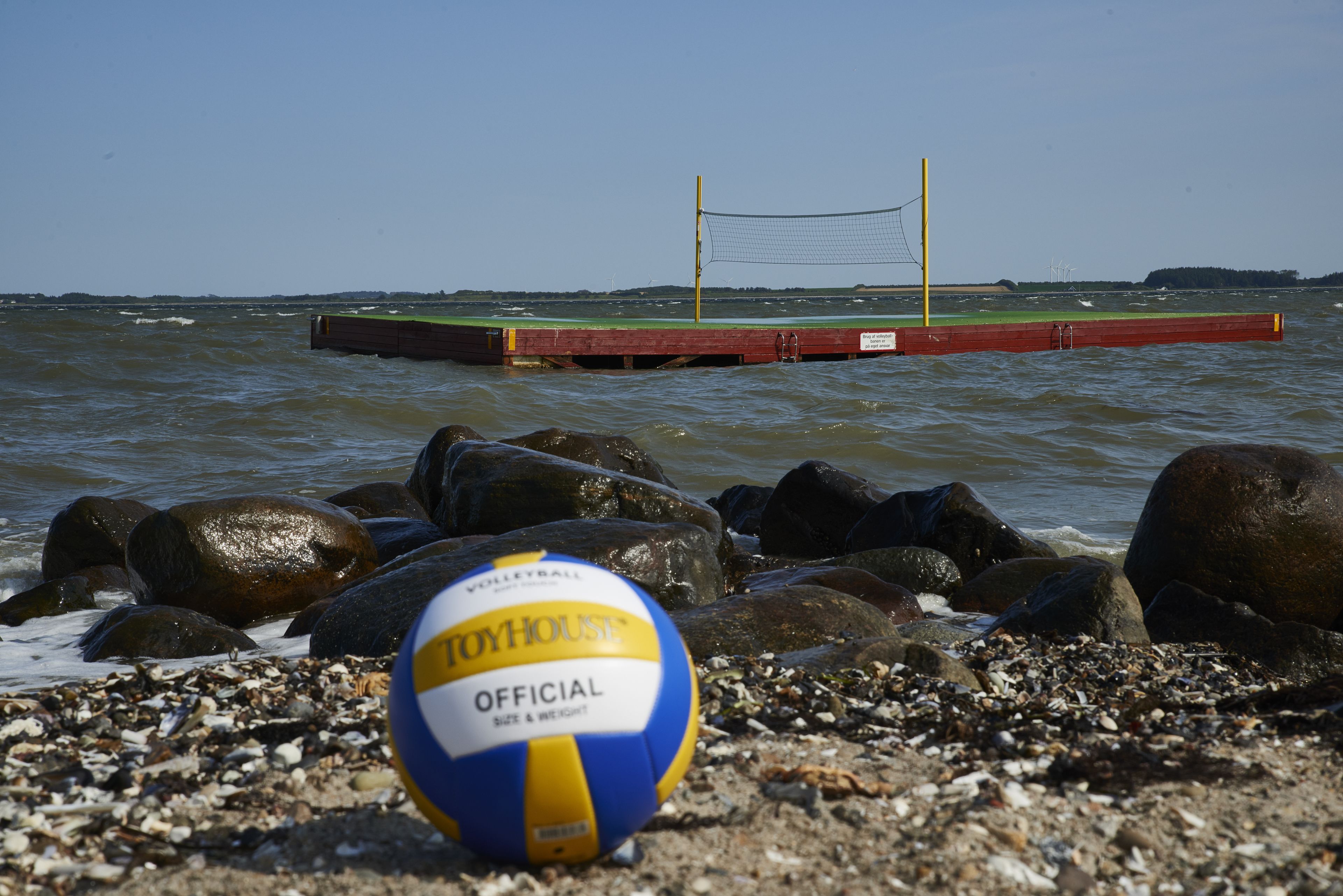 En strandvolleyboll på en stenstrand med ett volleybollnät i bakgrunden.