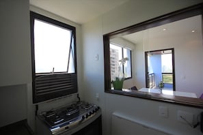 A kitchen with a gas stove, a window, and a large mirror reflecting the room. - Senna 1804 (Rio de Janeiro)