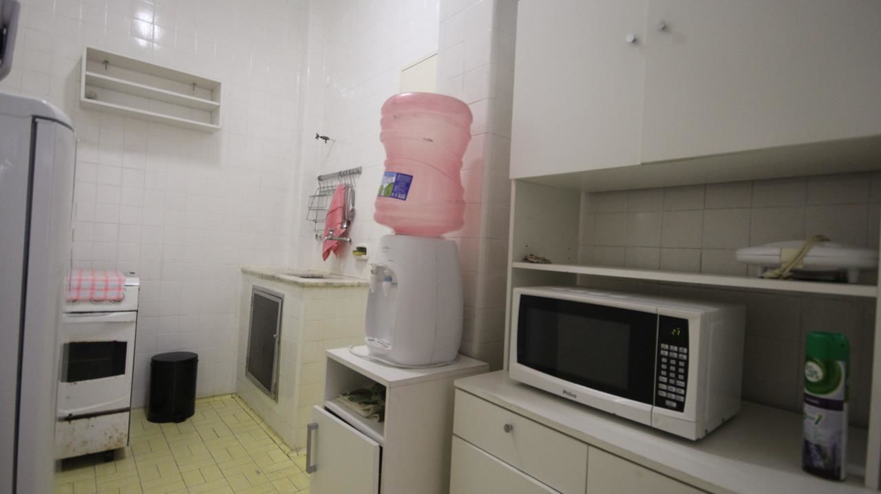 Una cocina pequeña con microondas, dispensador de agua, lavamanos y refrigerador.