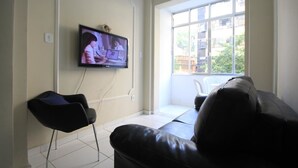 Ein Wohnzimmer mit einem wandmontierten Flachbildfernseher, einer schwarzen Ledersofa und einem schwarzen Sessel.