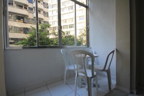 A small room with a window overlooking a building and greenery. There are two white plastic chairs and a small table. - Ferreira 201 (Rio de Janeiro)