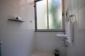 A small bathroom with white tiles, a window, a shower, a sink, and a toilet. - Ferreira 201 (Rio de Janeiro)