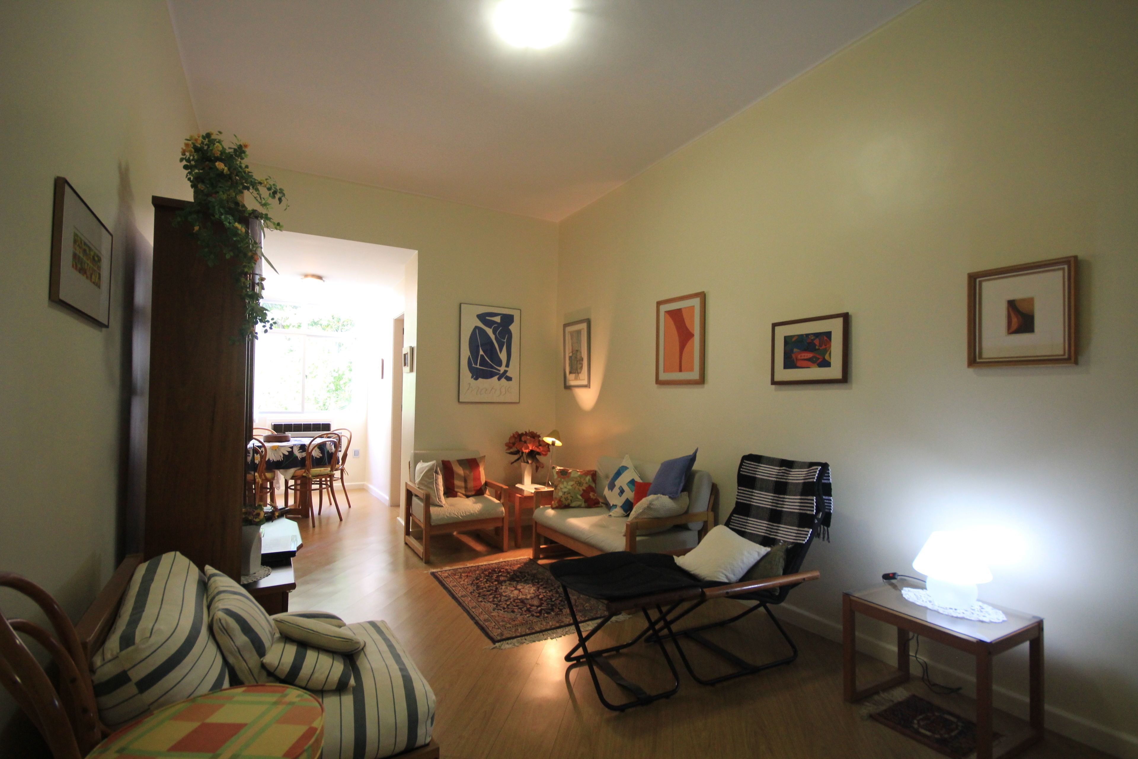 Un salon avec un canapé, des fauteuils, une table basse et une lampe. Des tableaux encadrés ornent le mur.