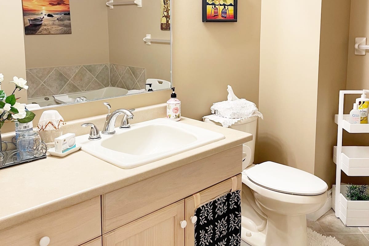 A modern bathroom with a large mirror, dual sinks, a toilet, and a small shelf with toiletries.