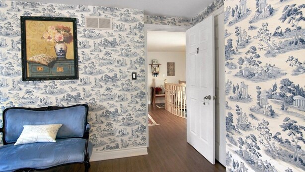 A room with blue and white patterned wallpaper, a blue sofa with a white cushion, and a door leading to another room. - Cobblestone Bed and Breakfast (Niagara-on-the-Lake)