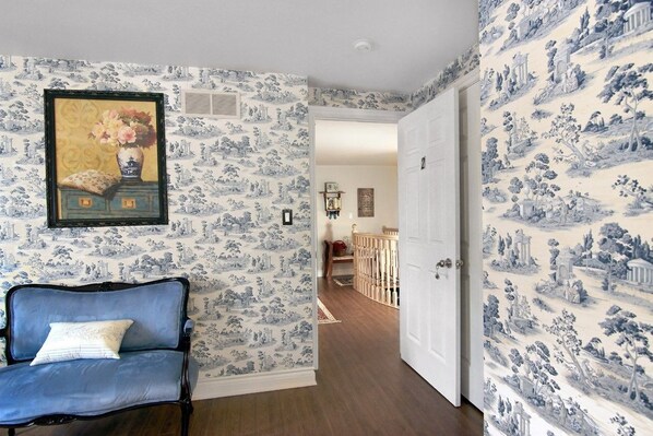 A room with blue and white patterned wallpaper, a blue sofa with a white cushion, and a door leading to another room. - Cobblestone Bed and Breakfast (Niagara-on-the-Lake)