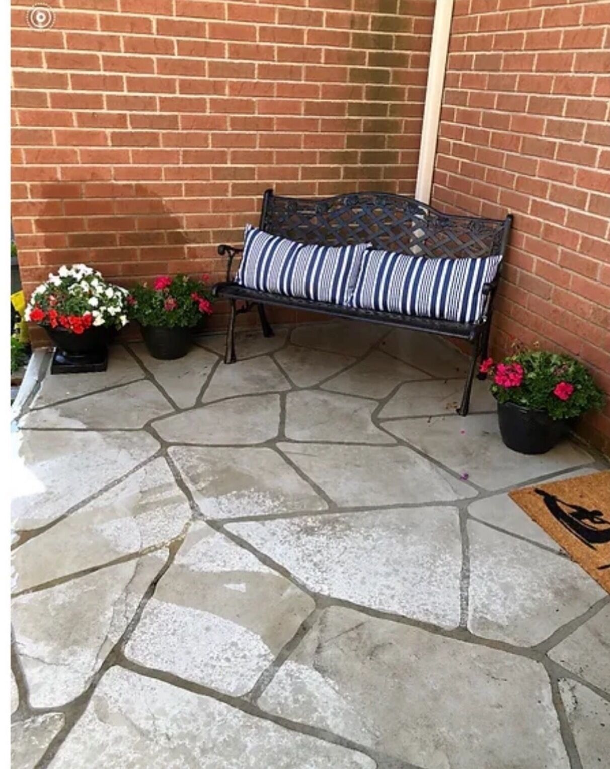 Un patio de piedra con un banco de metal y plantas en macetas.