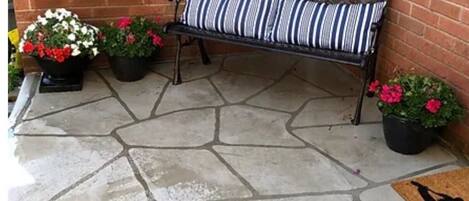 Un patio de piedra con un banco de metal y plantas en macetas.