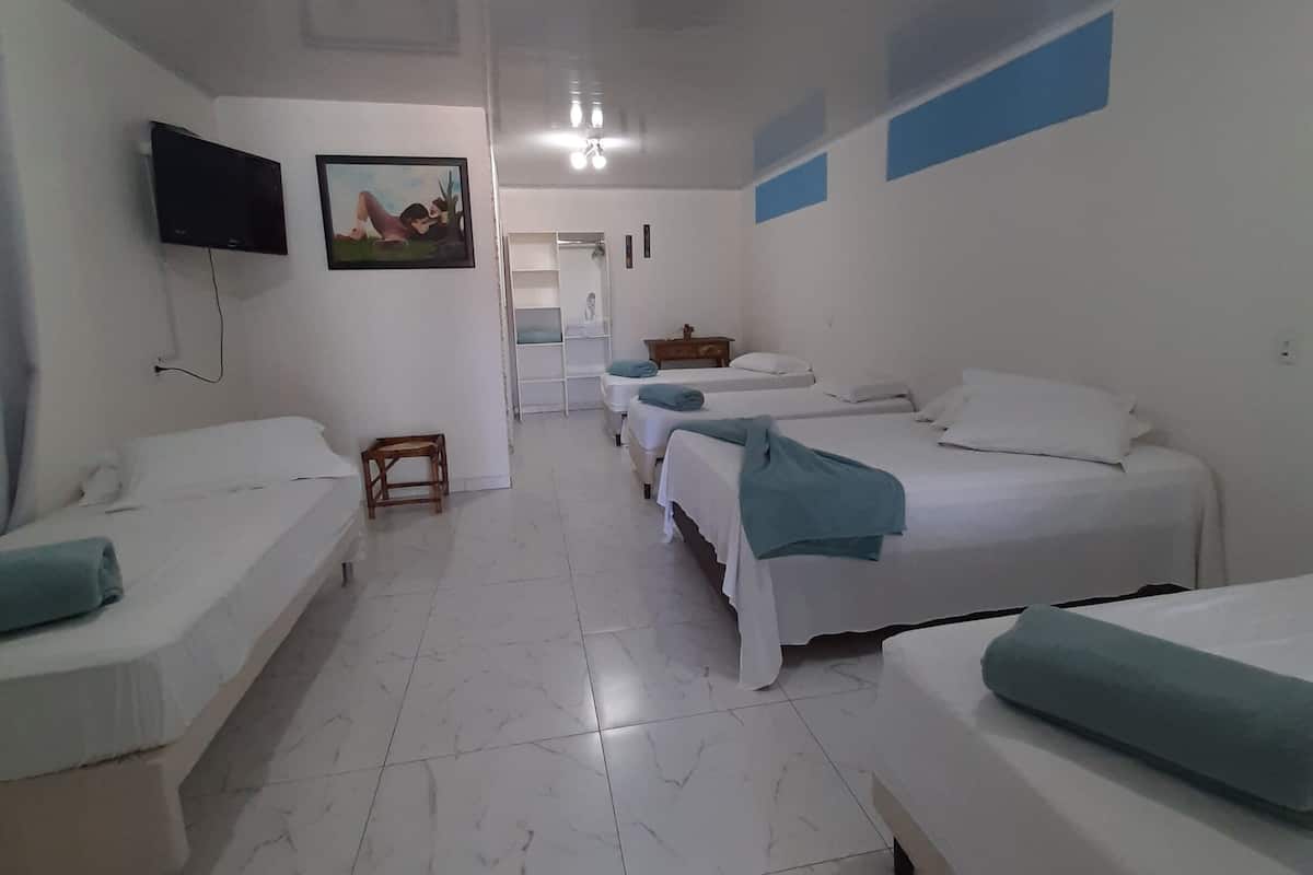 A hotel room with four single beds, a TV mounted on the wall, a small wooden stool, and a painting.