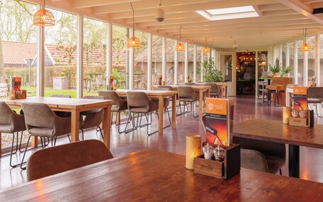 A spacious indoor dining area with wooden tables and chairs, large windows, and hanging pendant lights.