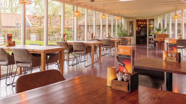 A spacious indoor dining area with wooden tables and chairs, large windows, and hanging pendant lights. - Landhotel Diever (Diever)