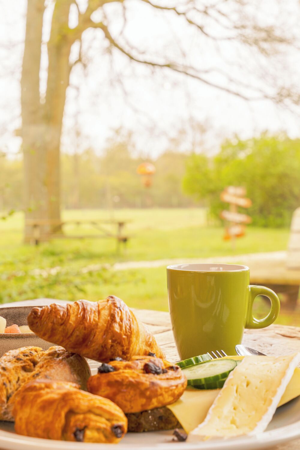 Een ontbijttafel met croissants, kaas en een groene kop.