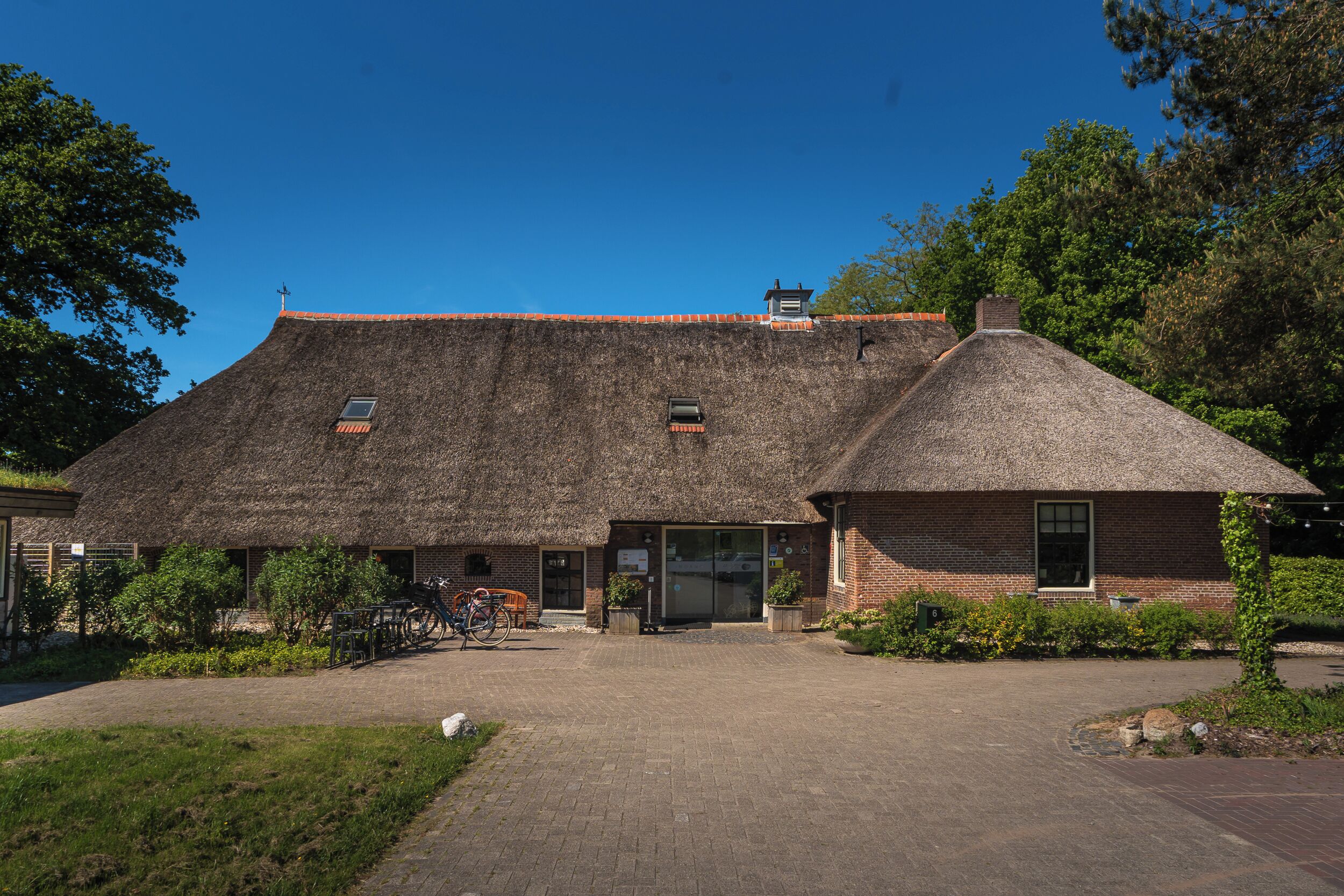 A brick building with a thatched roof, a small attached structure, and a paved entrance area.