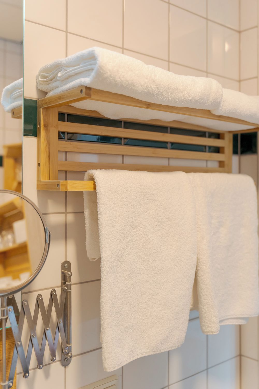 Een badkamer met een houten handdoekhouder met twee witte handdoeken, een spiegel en een handdoekwarmer.
