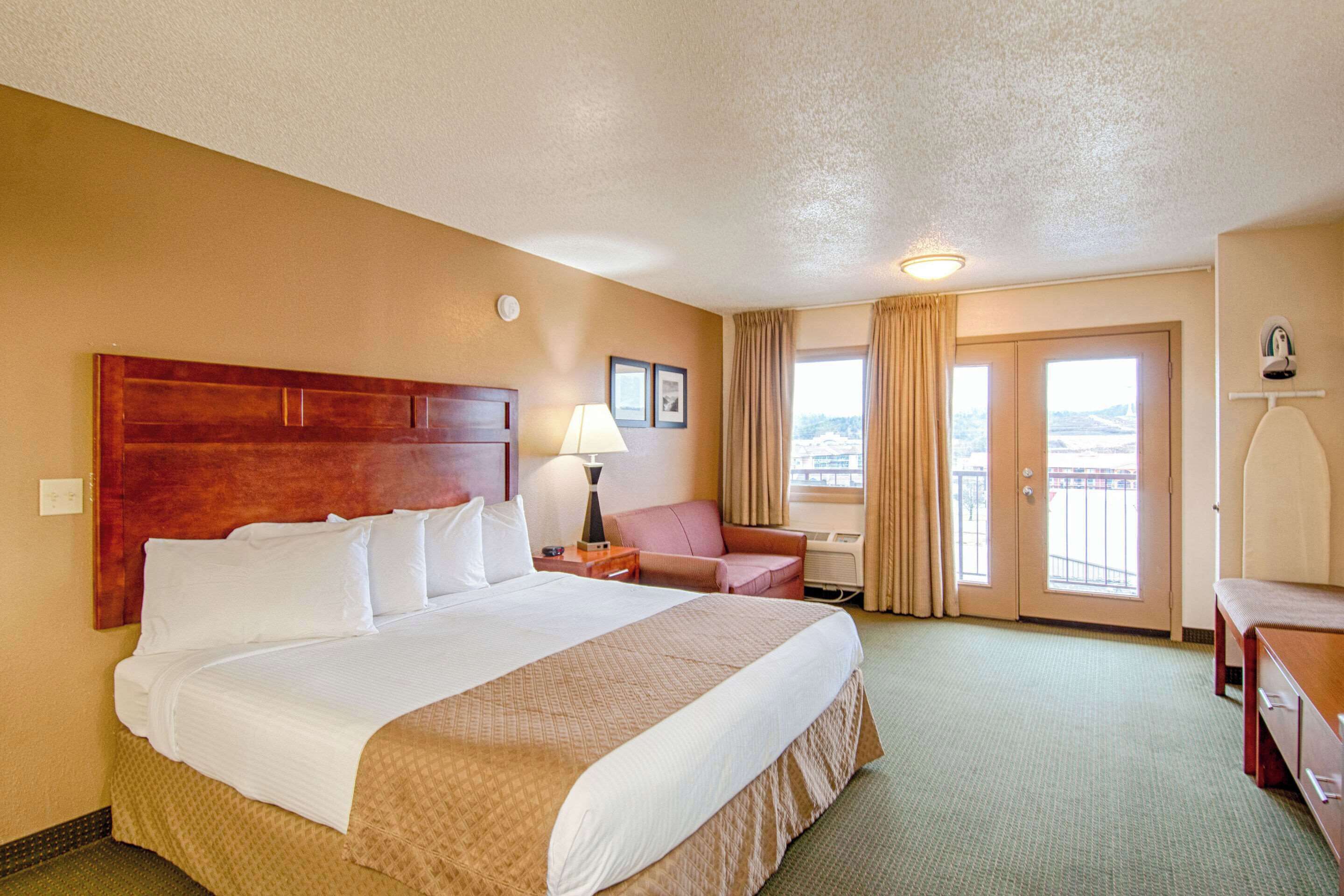 A hotel room with a large bed, a desk, a chair, and a view of the outdoors through the door.