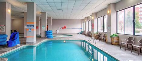 An indoor swimming pool with clear signage, including a 'No Diving' warning, and a seating area with chairs and potted plants.