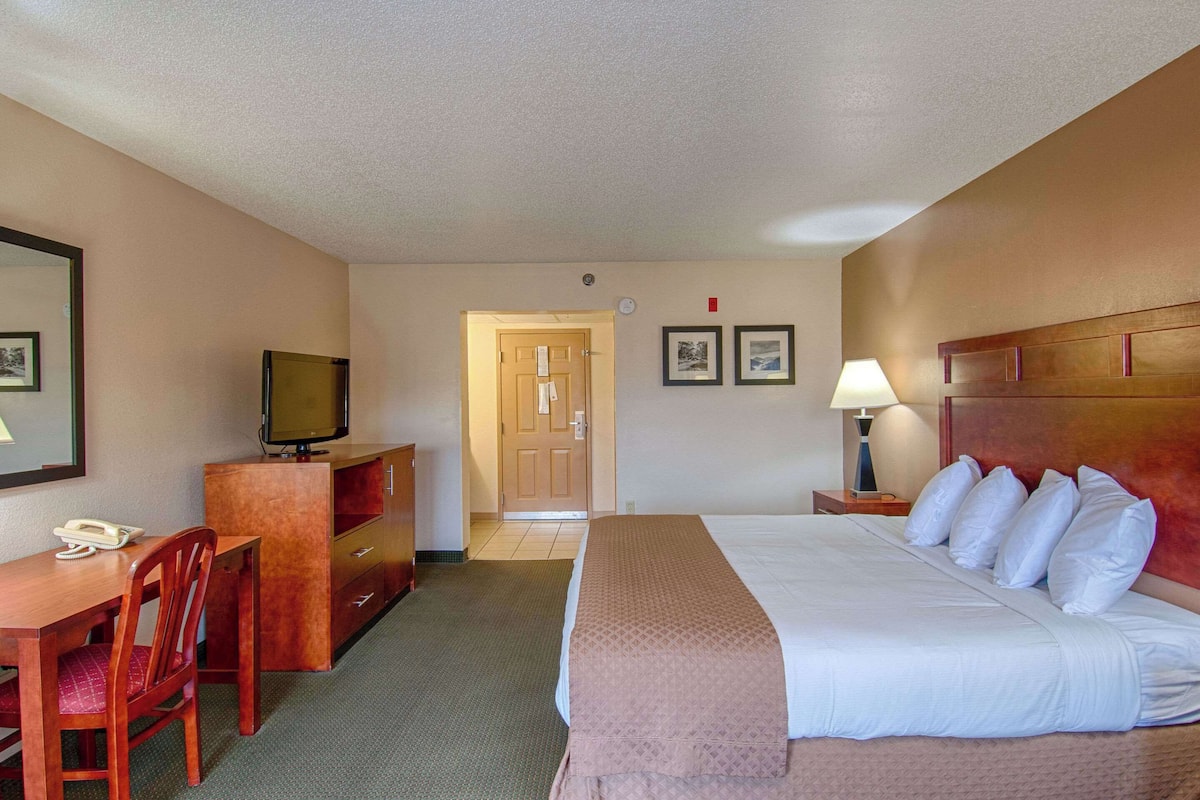 A hotel room with a bed, a desk with a telephone, a television, a dresser, and a door leading to another room.