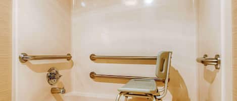 A bathtub with a wheelchair ramp, grab bars, and a handheld showerhead.