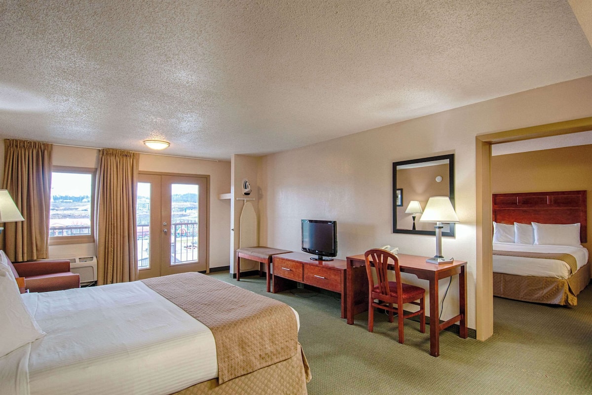 A hotel room with a bed, a desk with a television, a chair, and a window with curtains.