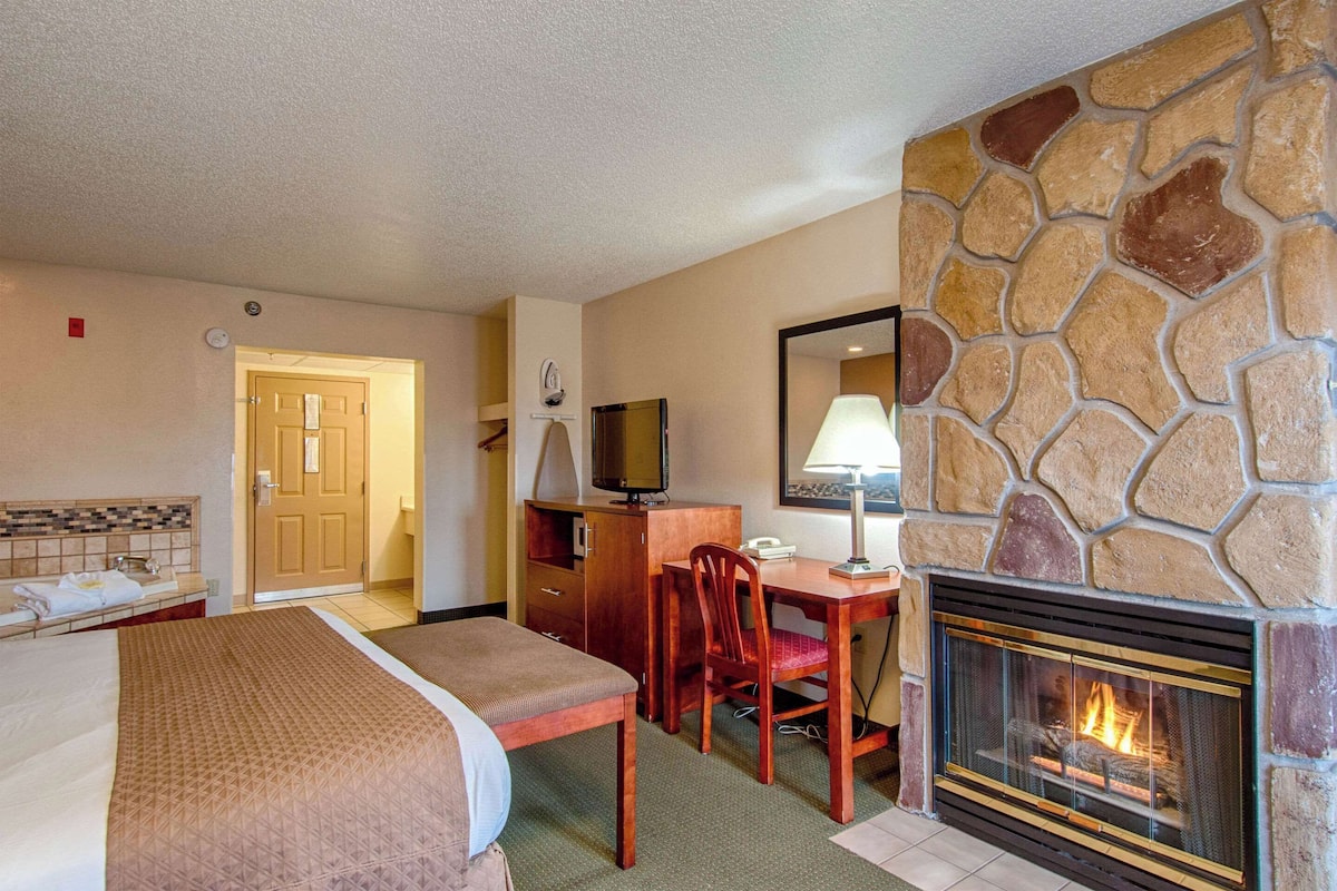 A hotel room with a bed, a desk, a chair, a television, a fireplace, and a stone wall.