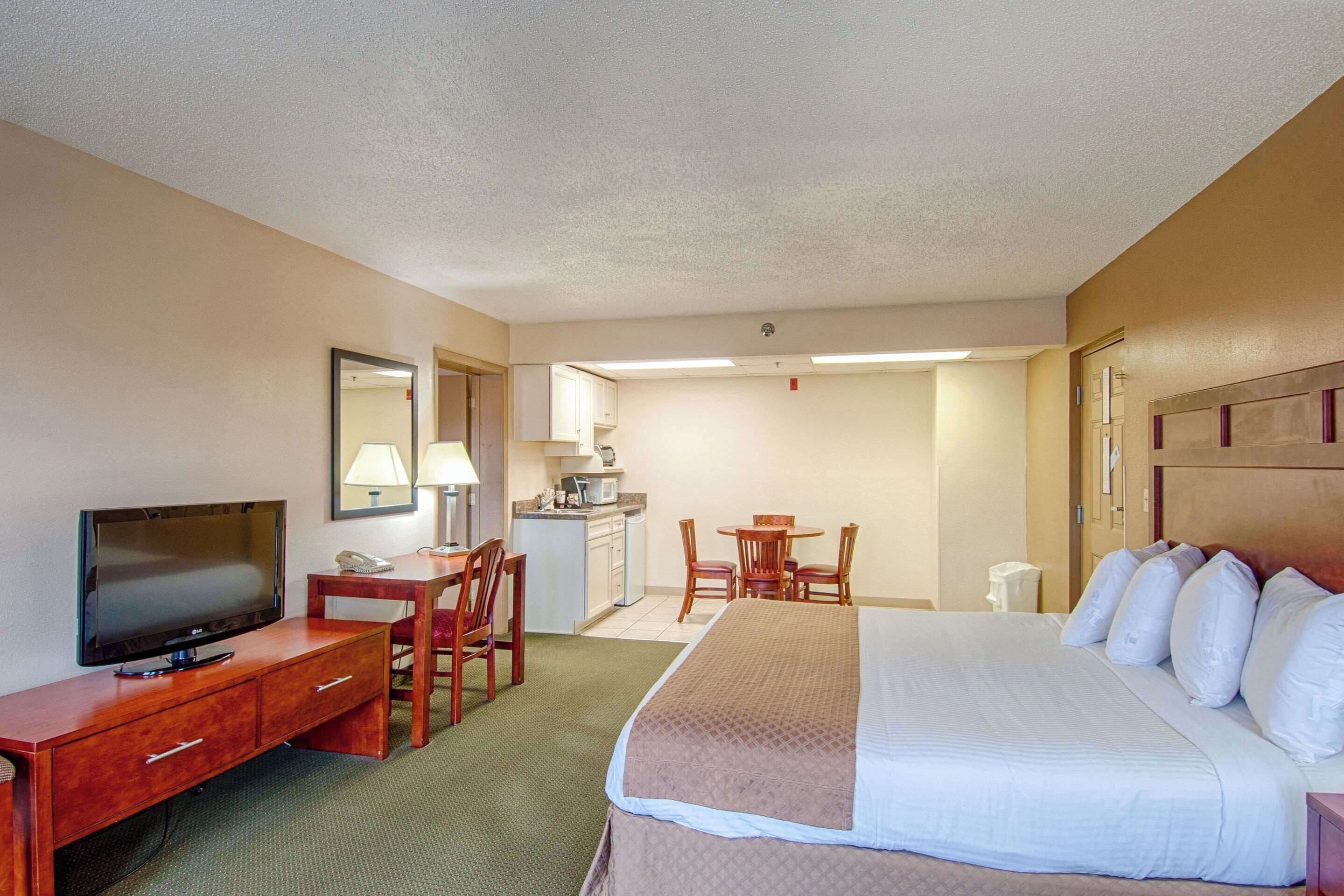 A hotel room with a bed, a desk with a TV, a dining area, and a kitchenette.