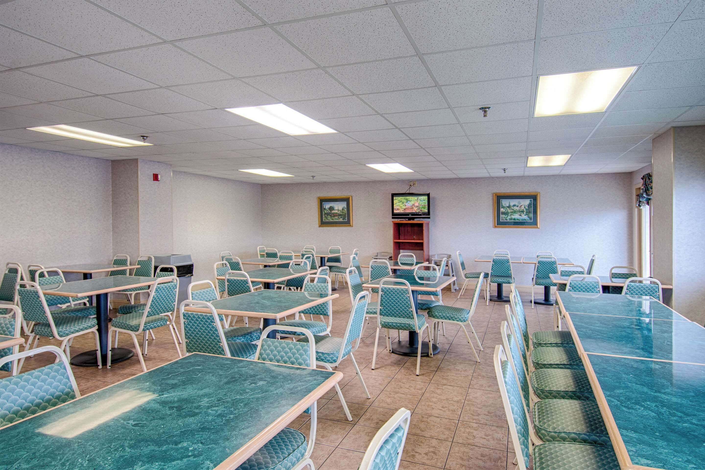 A dining area with multiple tables and chairs, a television mounted on the wall, and framed pictures on the walls.