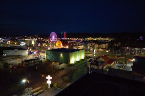 A nighttime view of a cityscape with illuminated buildings, a prominent Ferris wheel, and a large industrial structure.