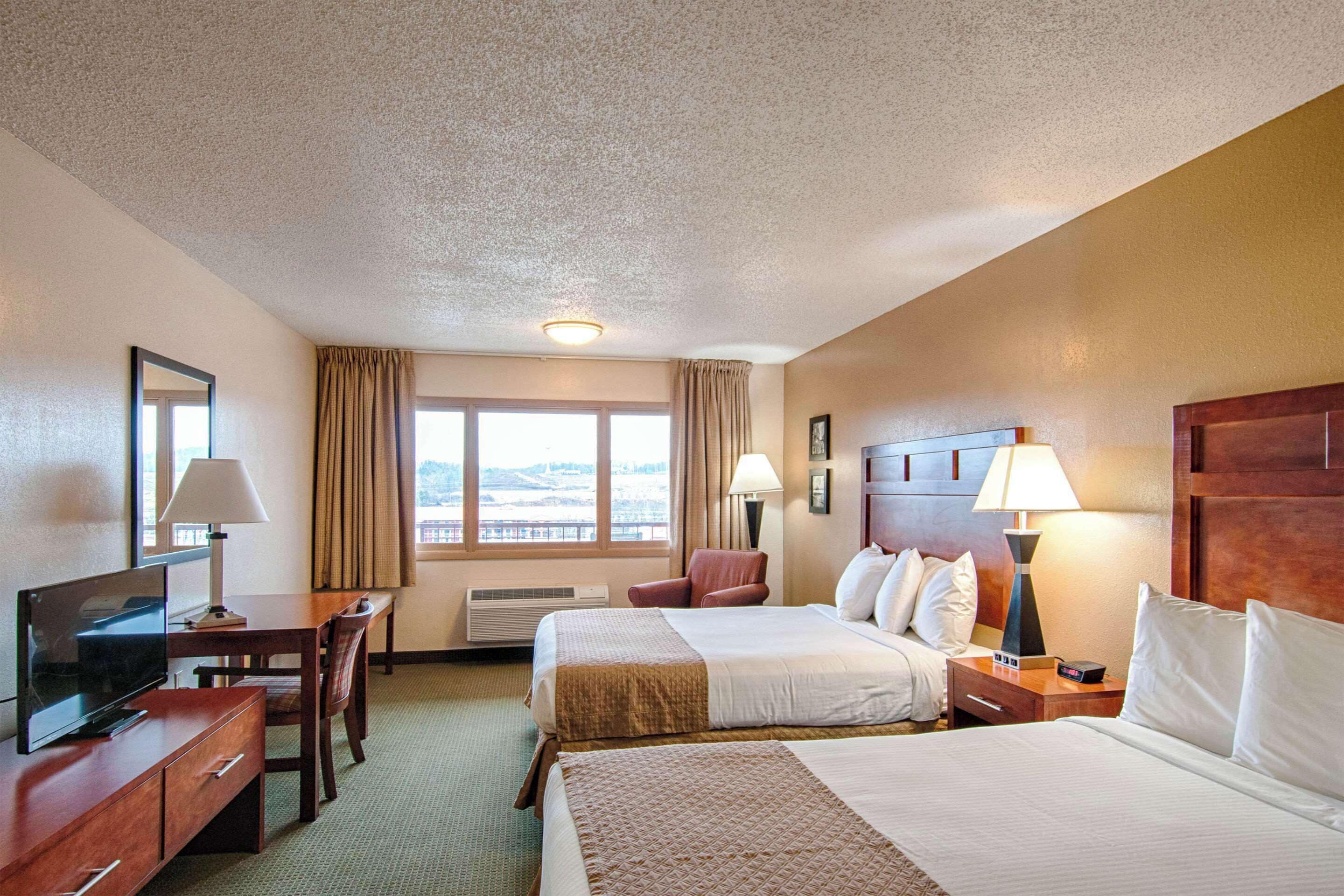 A hotel room with two beds, a desk with a TV, a chair, and a window with curtains.