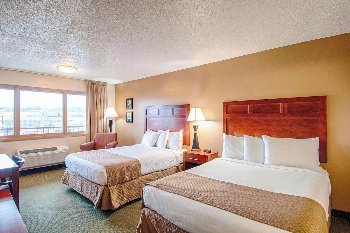 A hotel room with two beds, a desk, a chair, and a window with a city view.