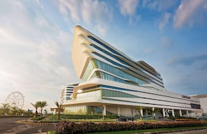A modern hotel with a unique curved facade, multiple floors, and a prominent entrance with a covered walkway.