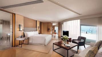 Una habitación de hotel moderna con una cama grande, una zona de estar con una mesa de centro, un televisor y vistas al mar.