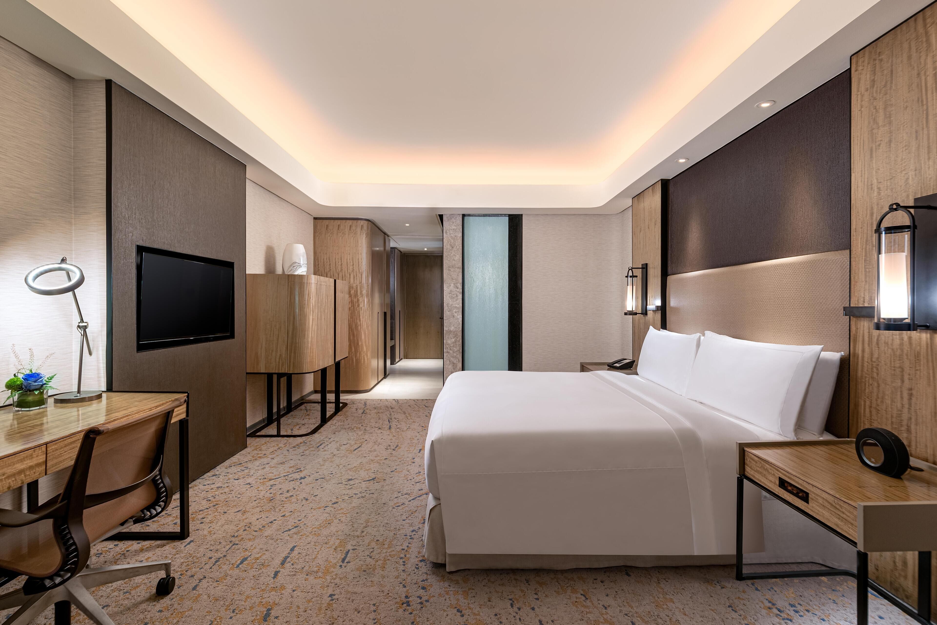 Una habitación de hotel moderna con una cama grande, un escritorio con una silla, un televisor de pantalla plana y una lámpara de escritorio.