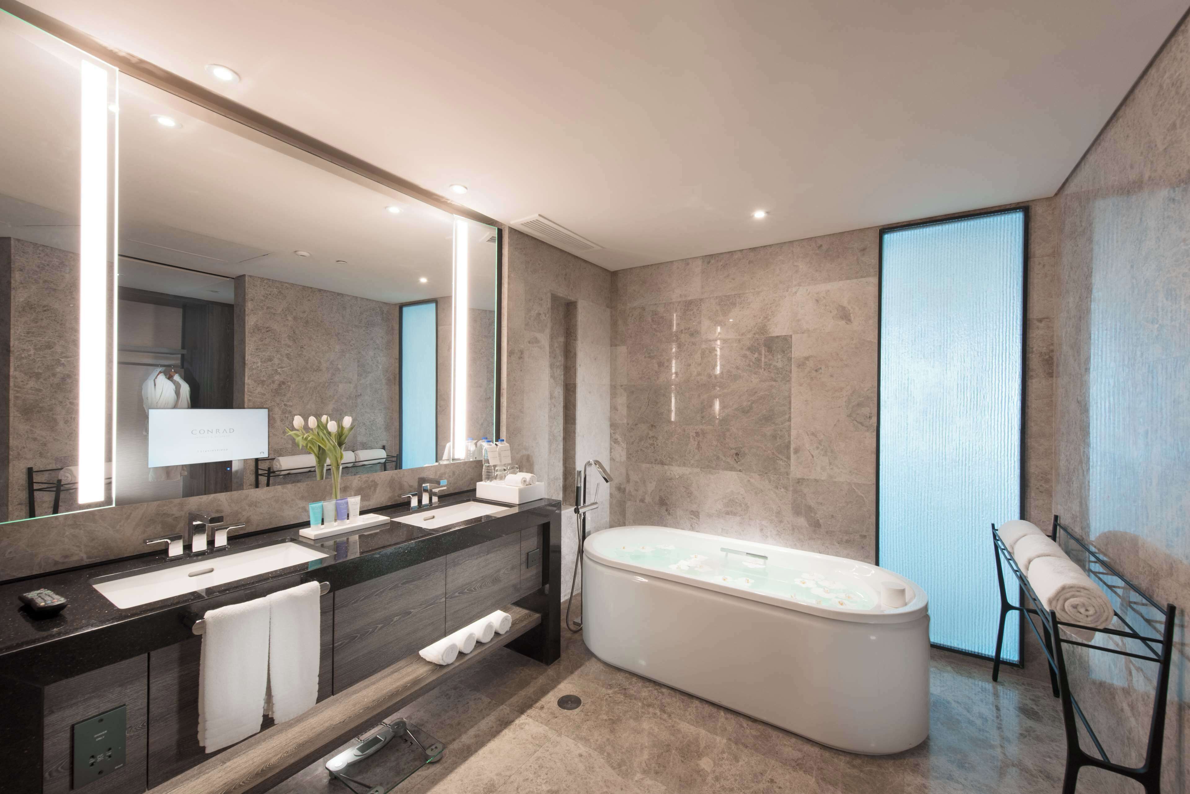 A modern bathroom with a large mirror, a bathtub, and a vanity with a sink and towel rack.