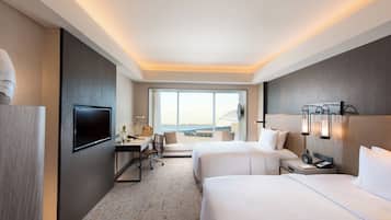 A hotel room with a large window, two beds, a desk, and a TV.