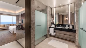 Un baño de hotel moderno con cabina de ducha de vidrio, un espejo grande y tocador con encimera negra.