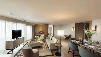 A modern hotel room with a flat-screen TV, a sofa, a dining table set for four, and a coffee table.