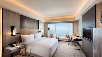 Habitación de hotel con una cama grande, un escritorio con silla, un sofá, un televisor y un ventanal con vistas.