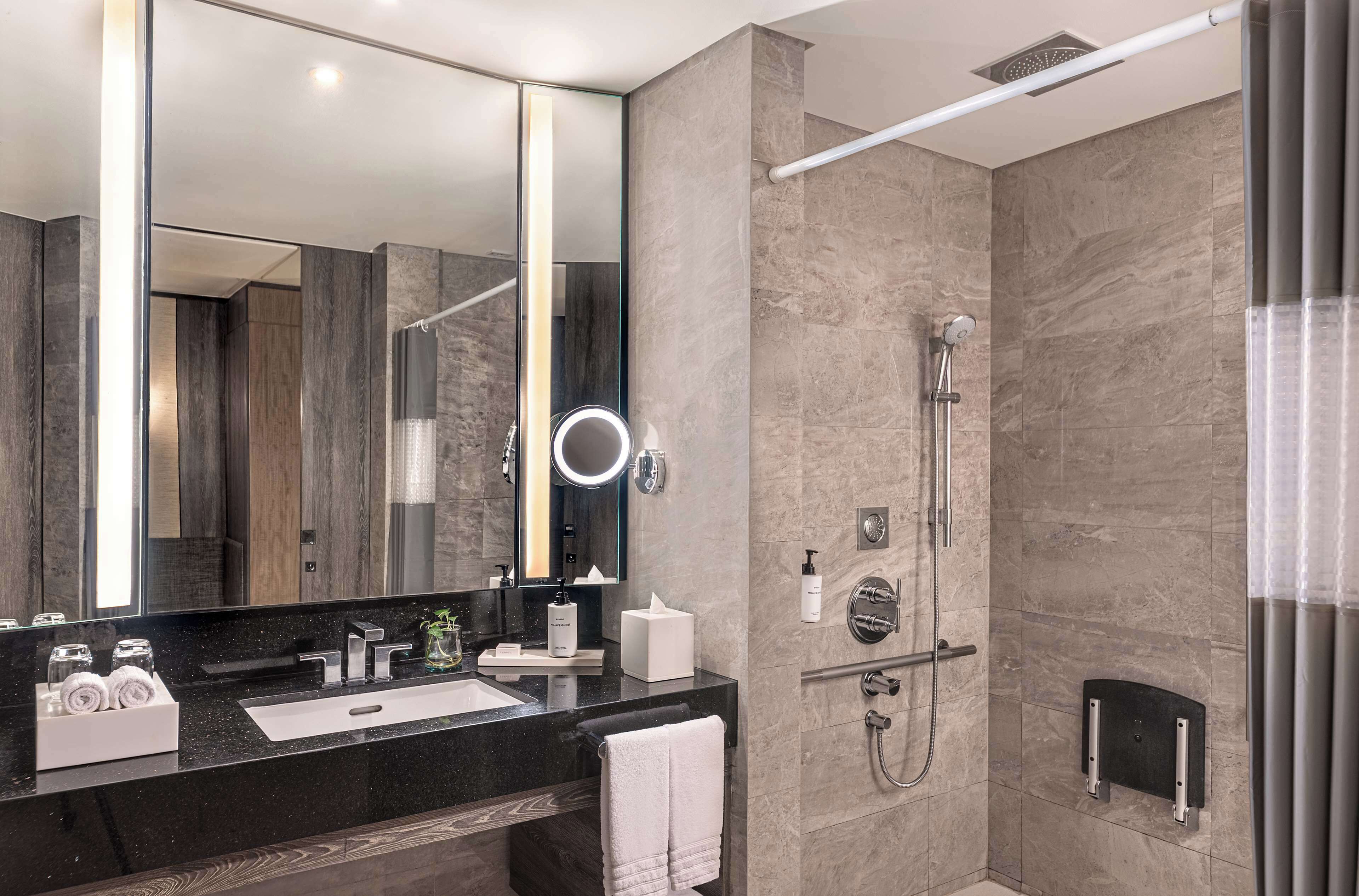 Un baño moderno con un espejo grande, una encimera negra, una ducha con cabezal de ducha manual y un perchero para toallas.