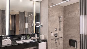 Un baño moderno con un espejo grande, una encimera negra, una ducha con cabezal de ducha manual y un perchero para toallas.
