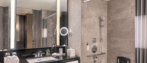 A modern bathroom with a large mirror, a black countertop, a shower with a handheld showerhead, and a towel rack.