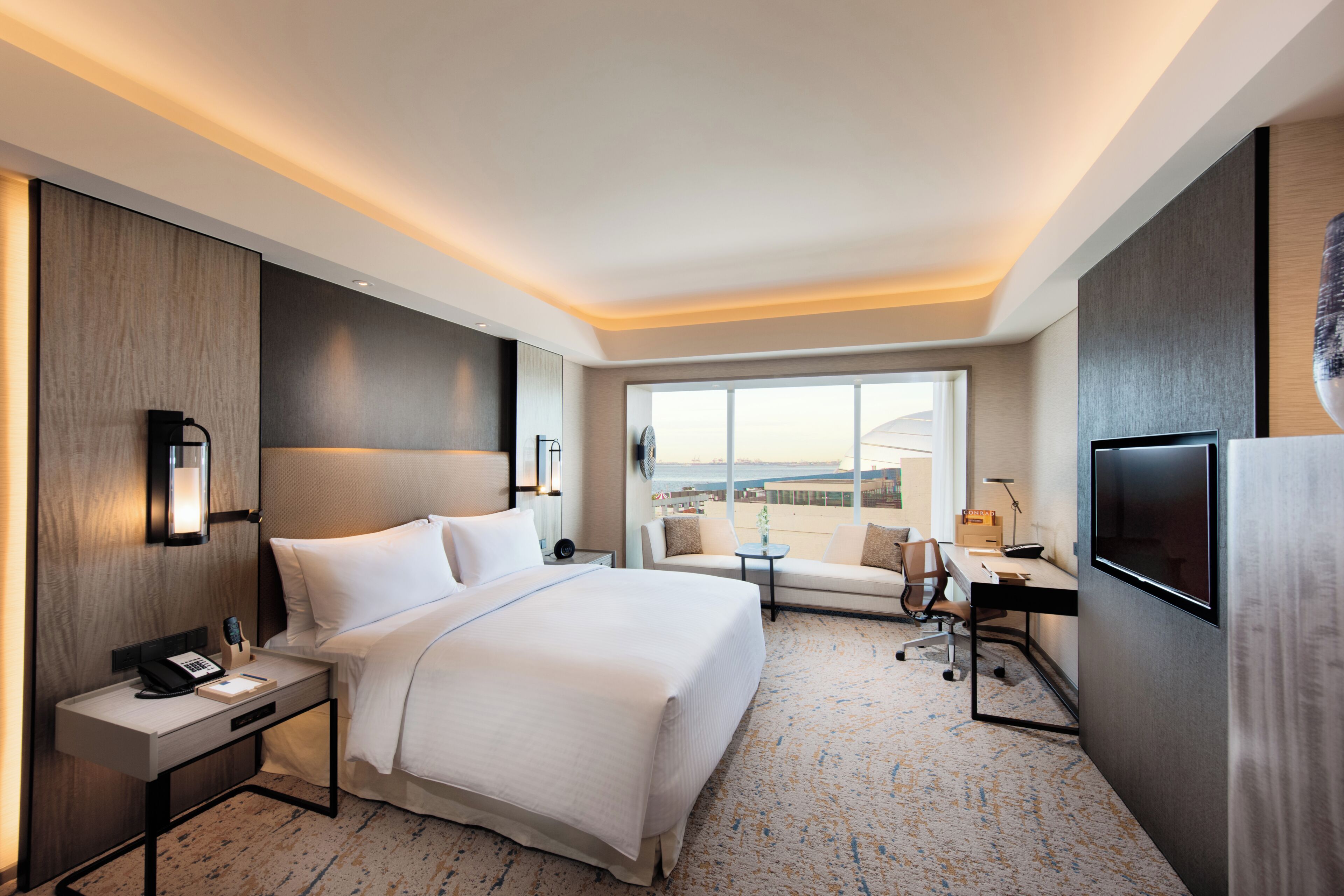 A hotel room with a large bed, a desk with a chair, a TV, and a window with a city view.