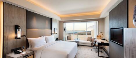A hotel room with a large bed, a desk with a chair, a TV, and a window with a city view.