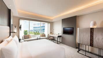 Habitación de hotel con una cama grande, un escritorio, una silla, un televisor y una ventana con vistas a edificios.