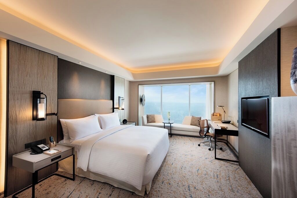 A hotel room with a large bed, a desk, a chair, a TV, and a window with a view.