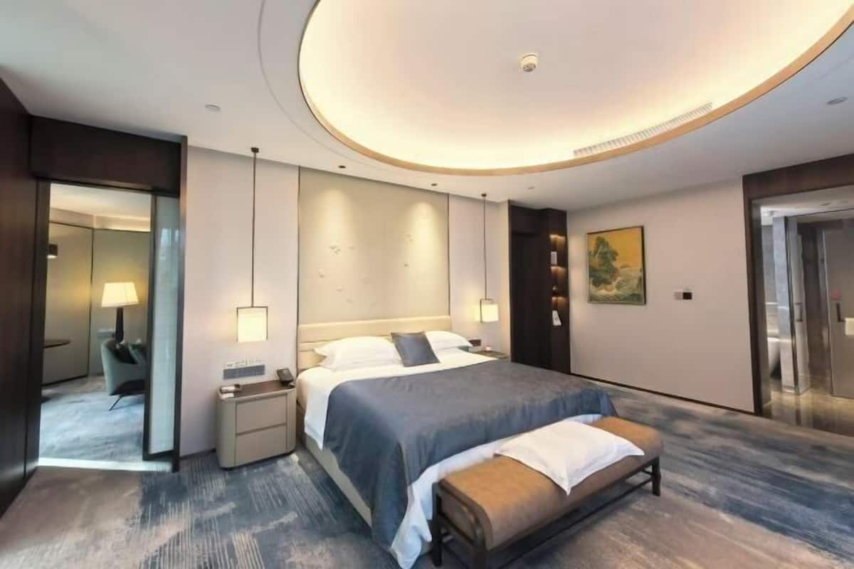 Une chambre d’hôtel moderne avec un grand lit, des tables de chevet, un banc, un miroir et un tableau au mur.