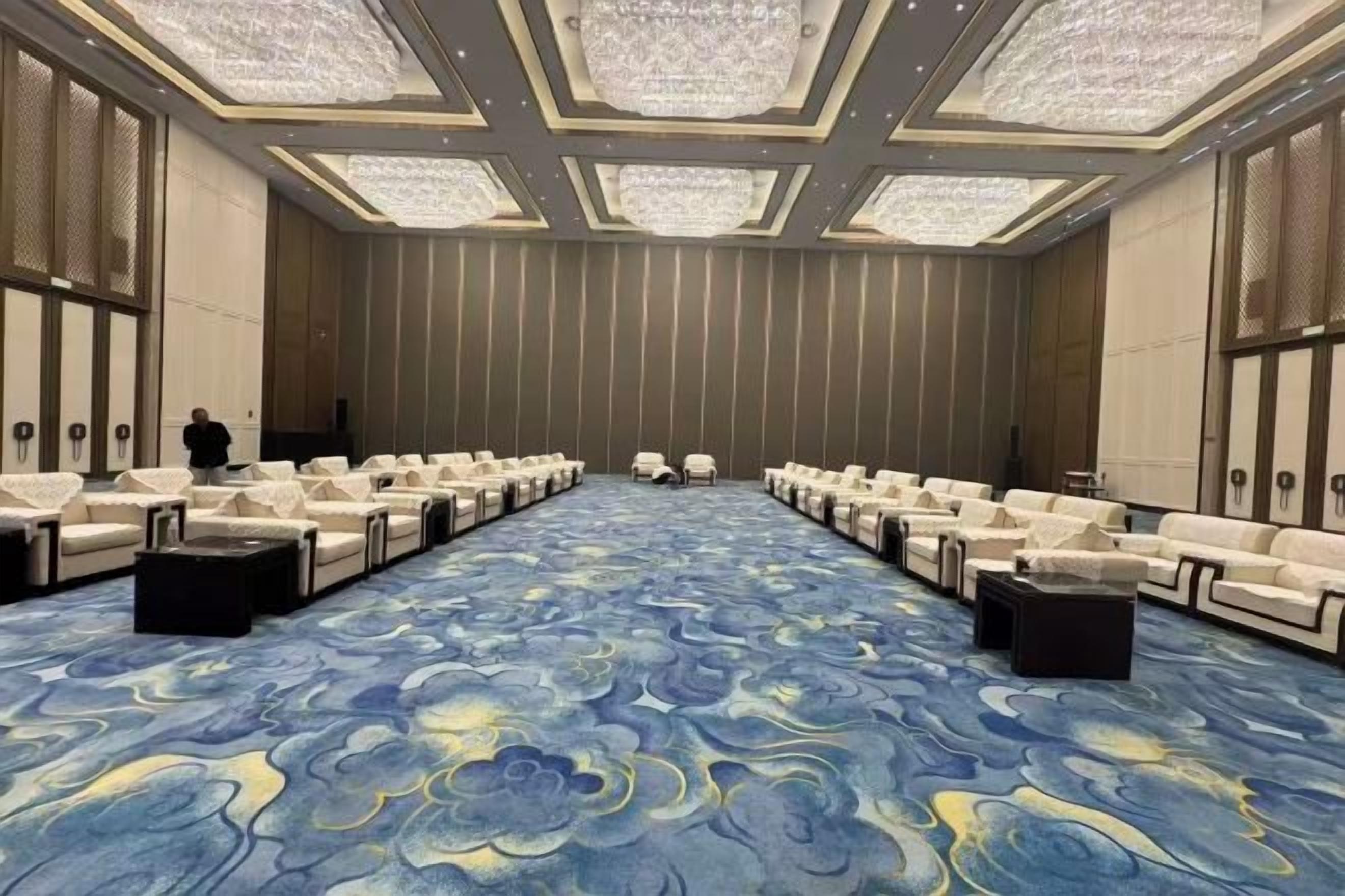 Un salón de conferencias con filas de sillas de cuero blancas, una alfombra estampada y una lámpara de araña grande.