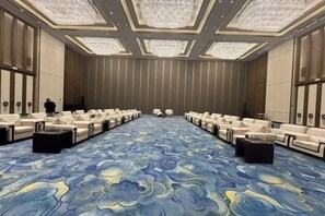 Un salón de conferencias con filas de sillas de cuero blancas, una alfombra estampada y una lámpara de araña grande.